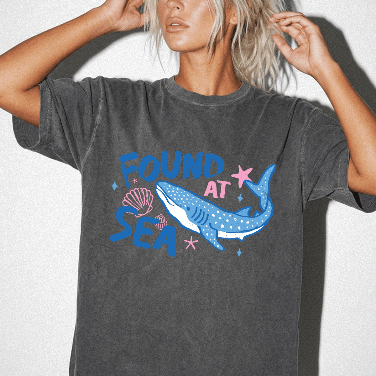 A woman wearing a gray t-shirt with a graphic design of a blue whale and seashells.