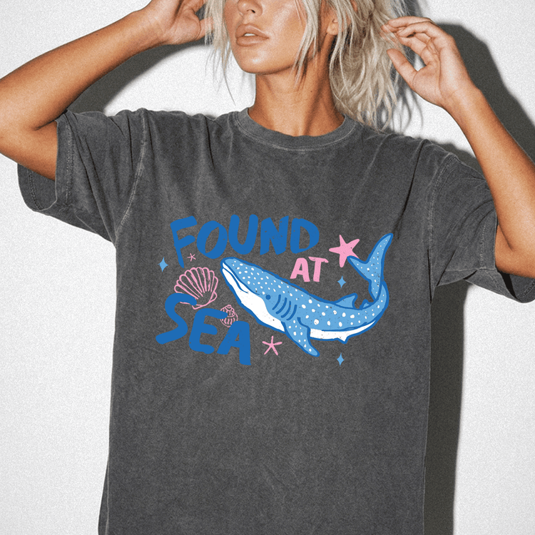A woman wearing a gray t-shirt with a graphic design of a blue whale and seashells.