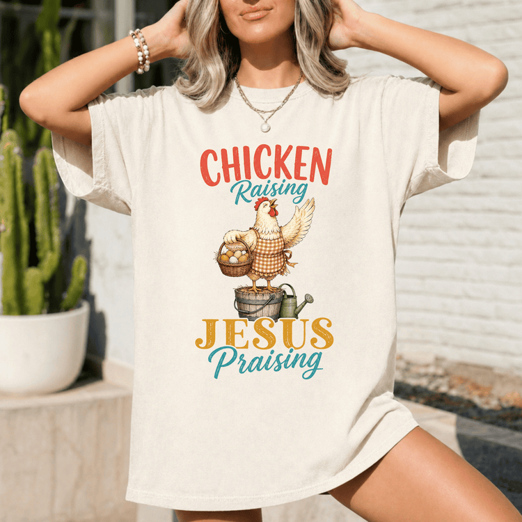 A woman wearing a white t-shirt with a graphic design of a chicken and the text "Chicken Raising Jesus Praising" printed on it.