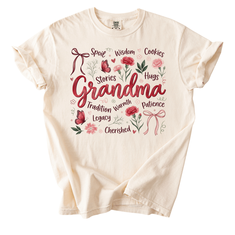 The image is a white t-shirt with a graphic design featuring the word "Grandma" surrounded by various words and illustrations such as stories, wisdom, cookies, roses, and more.