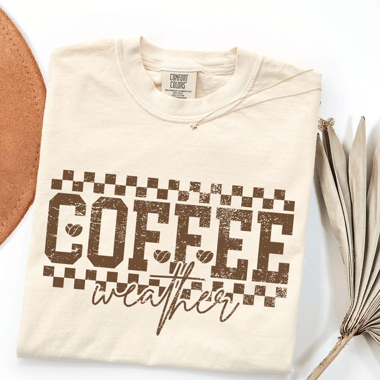 a beige t-shirt with a graphic design that says "COFFEE weather" in a distressed font.