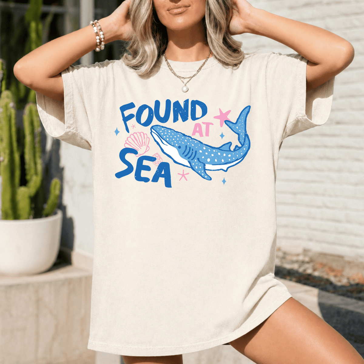 A woman wearing a white t-shirt with a graphic design of a blue whale and the text "FOUND AT SEA" printed on it.