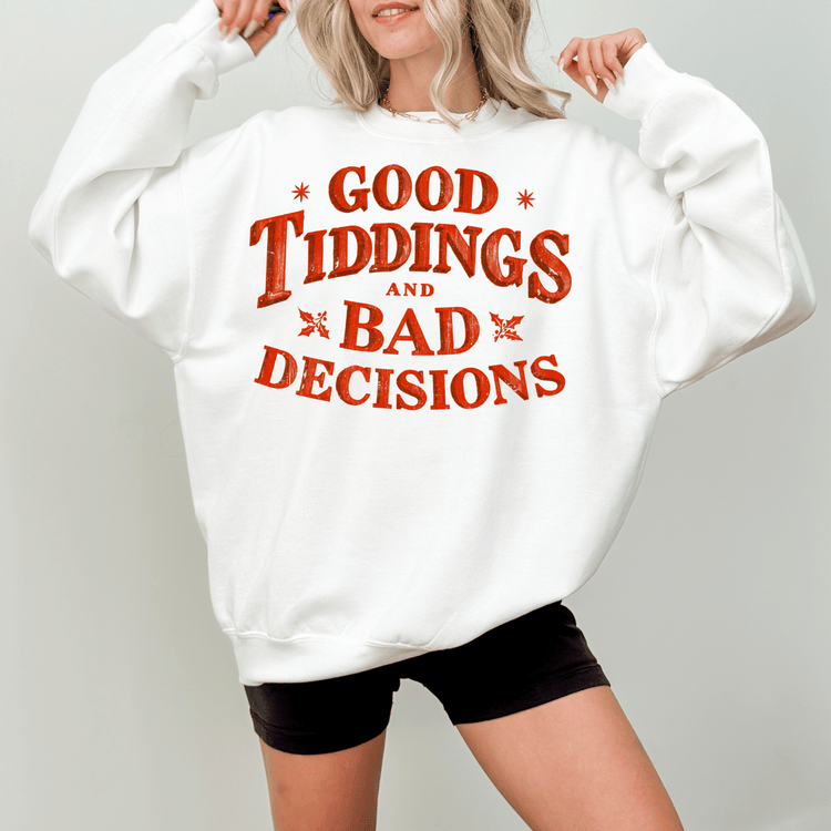 A woman wearing a white sweatshirt with the text "GOOD TIDDINGS AND BAD DECISIONS" printed on it.