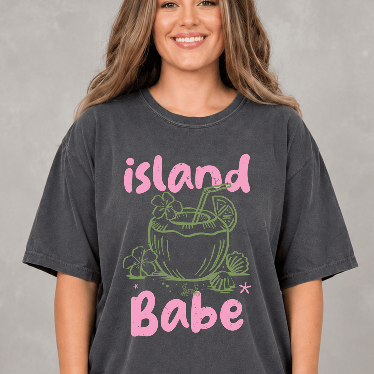 A woman wearing a gray t-shirt with a graphic design of a tropical drink and the text "island Babe" printed on it.