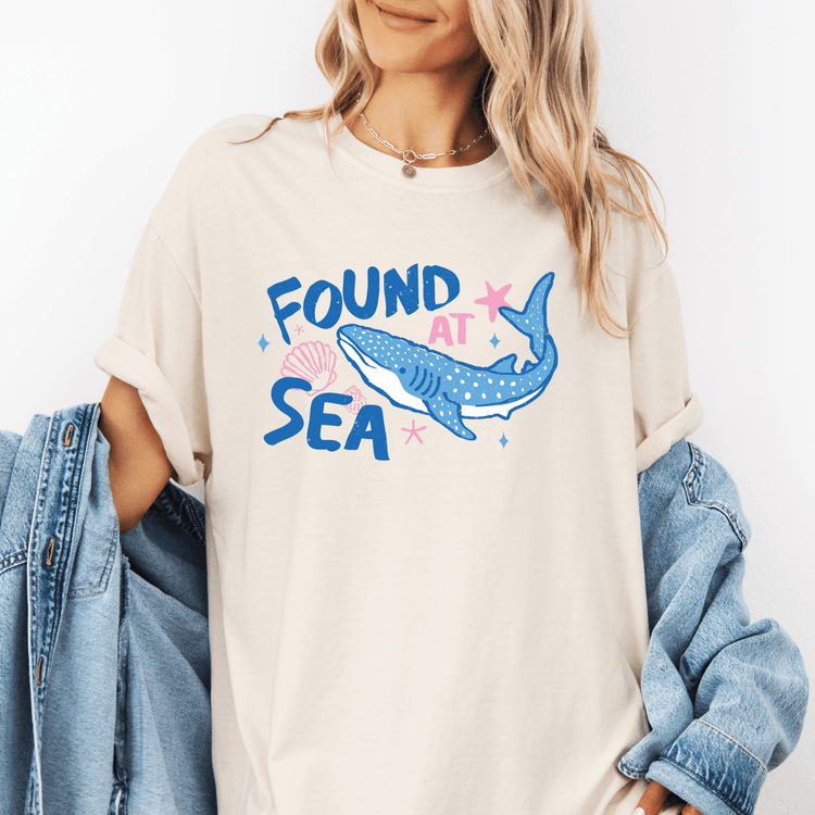 A woman wearing a white t-shirt with a graphic of a blue whale and the text "FOUND AT SEA" printed on it.