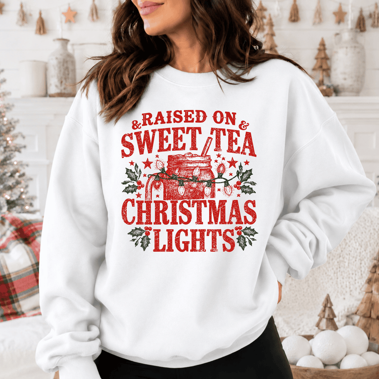 A woman wearing a white sweatshirt with a red and green graphic design that says "Raised on & Sweet Tea Christmas Lights".