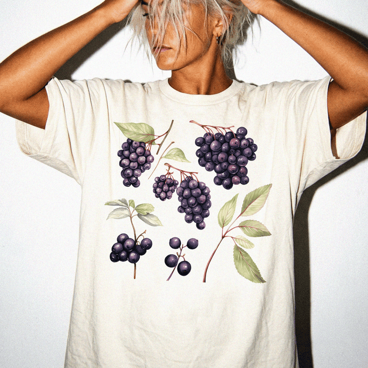 A person wearing a white t-shirt with a graphic design of various purple grapes and leaves.