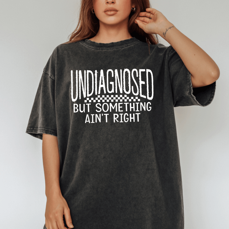 A woman wearing a black t-shirt with white text that says "UNDIAGNOSED BUT SOMETHING AIN'T RIGHT".
