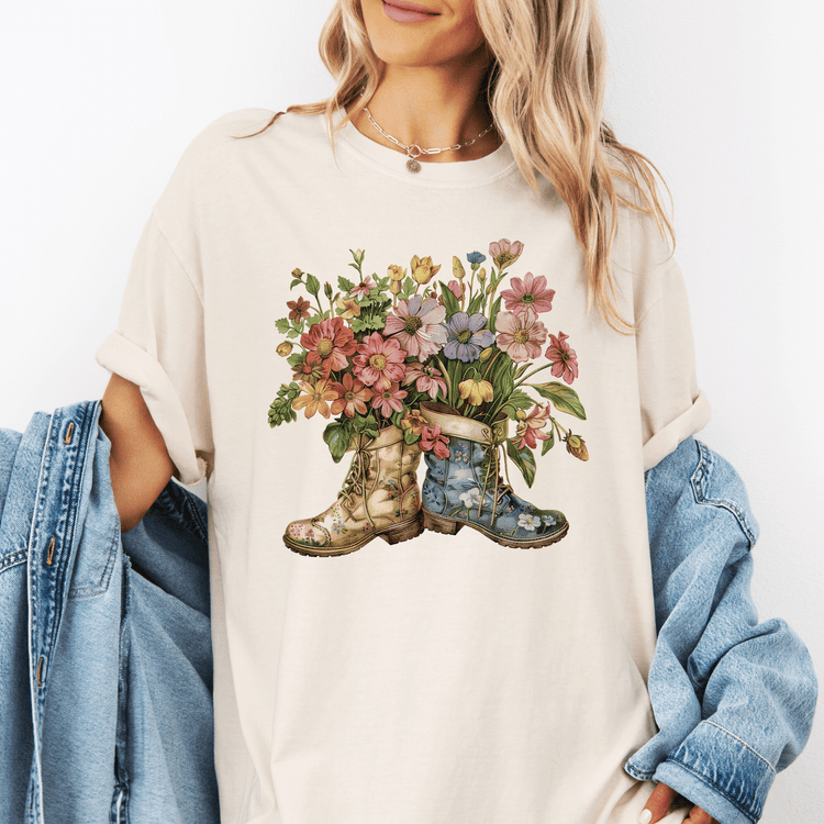 A woman wearing a white t-shirt with a floral design of two boots, one blue and one yellow, holding a bouquet of colorful flowers.