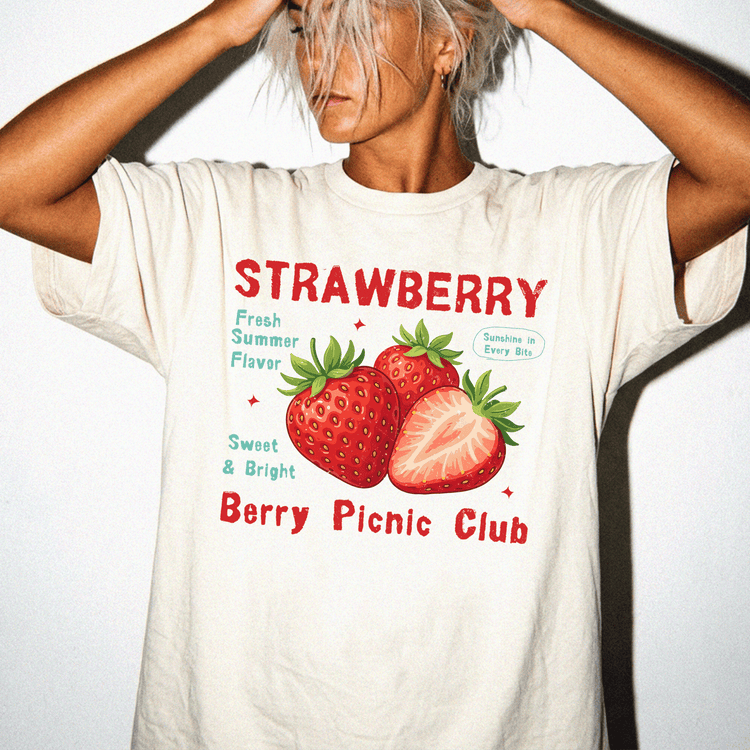 A person wearing a white t-shirt with a graphic design of strawberries and text promoting a berry picnic club.