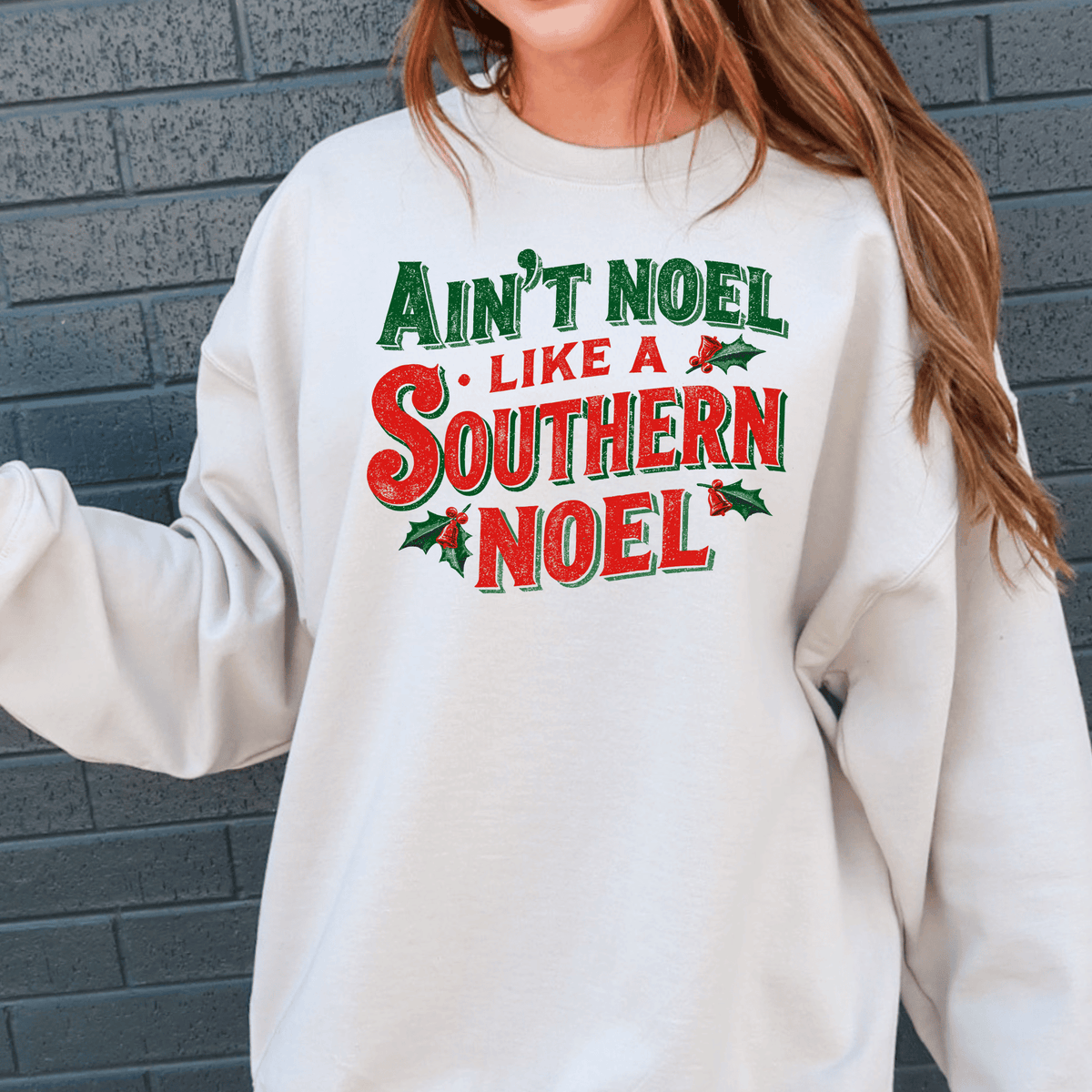 A white sweatshirt with a printed text design that says "Ain't Noel Like a Southern Noel" in red and green colors.