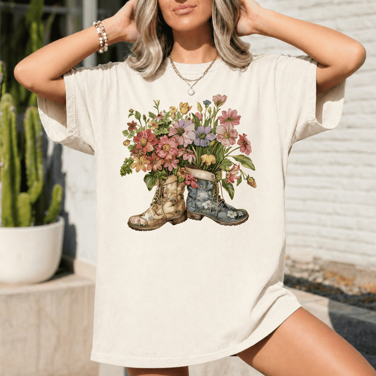 A woman wearing a white t-shirt with a floral design of two boots, one blue and one green, holding a bouquet of colorful flowers.