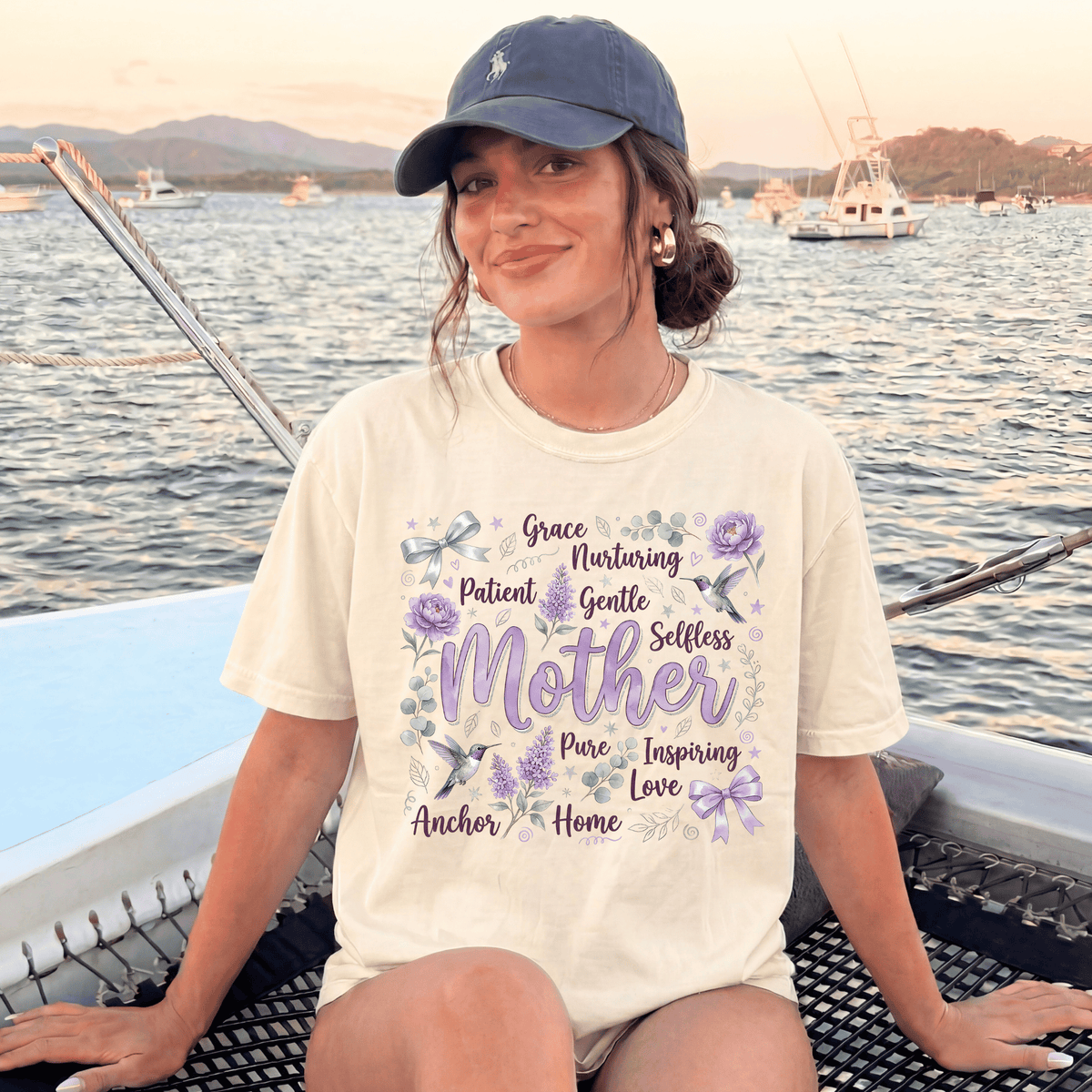 A woman wearing a white t-shirt with a graphic design and text, sitting on a boat in the water with mountains in the background.