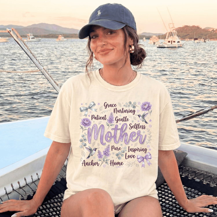 A woman wearing a white t-shirt with a graphic design and text, sitting on a boat in the water with mountains in the background.