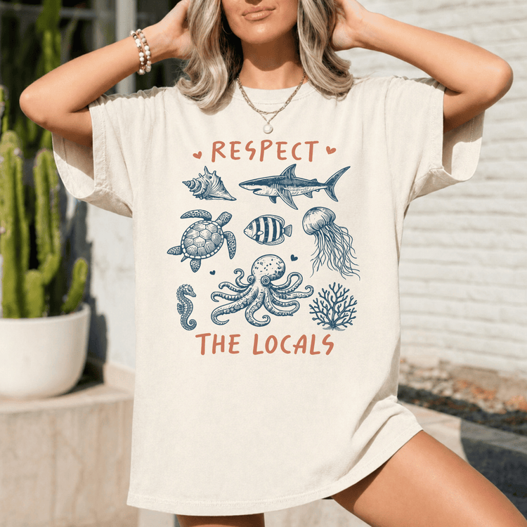A woman wearing a white t-shirt with a graphic design of marine life and the text "RESPECT THE LOCALS" printed on it.
