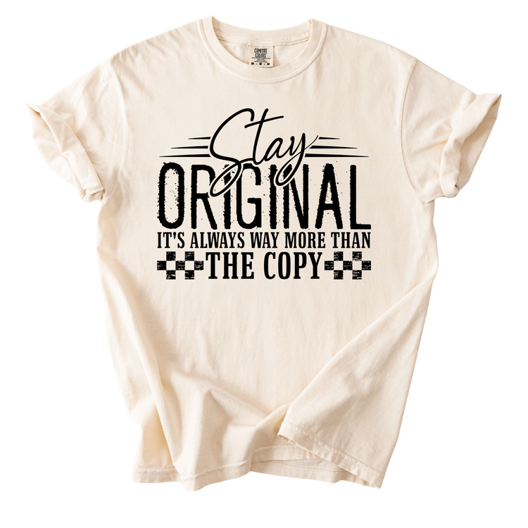A white t-shirt with a printed text design that reads "Stay original, it's always way more than the copy".