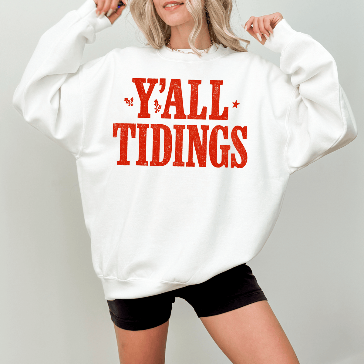 A woman wearing a white sweatshirt with the text "Y'ALL TIDINGS" printed on it.