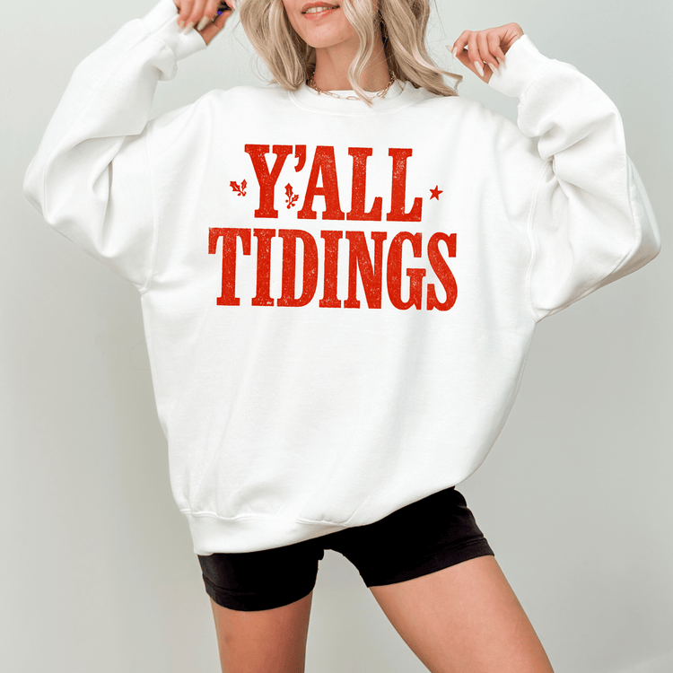 A woman wearing a white sweatshirt with the text "Y'ALL TIDINGS" printed on it.