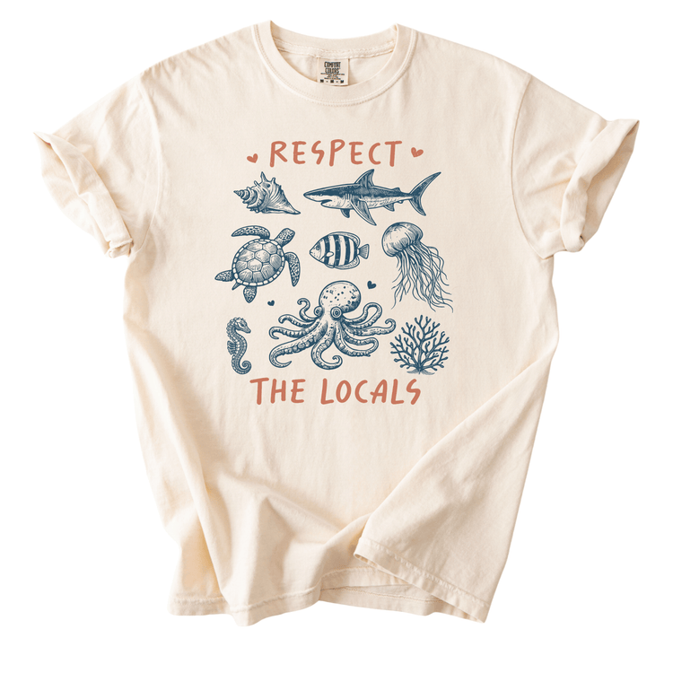 a white t-shirt with a graphic design depicting various marine life, including a shark, turtle, octopus, and jellyfish, along with the text "RESPECT THE LOCALS".