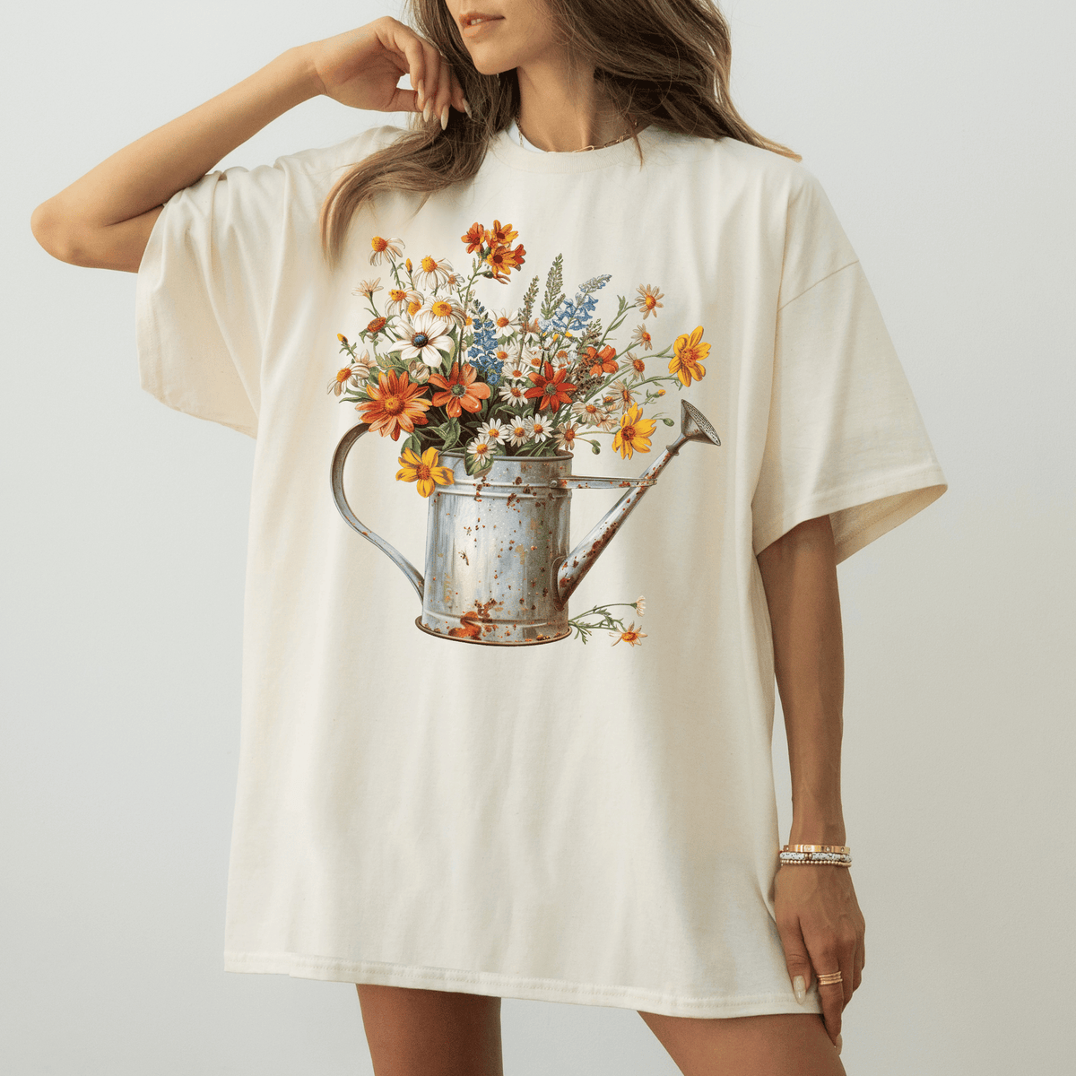 A woman wearing a white t-shirt with a printed image of a watering can filled with colorful flowers.