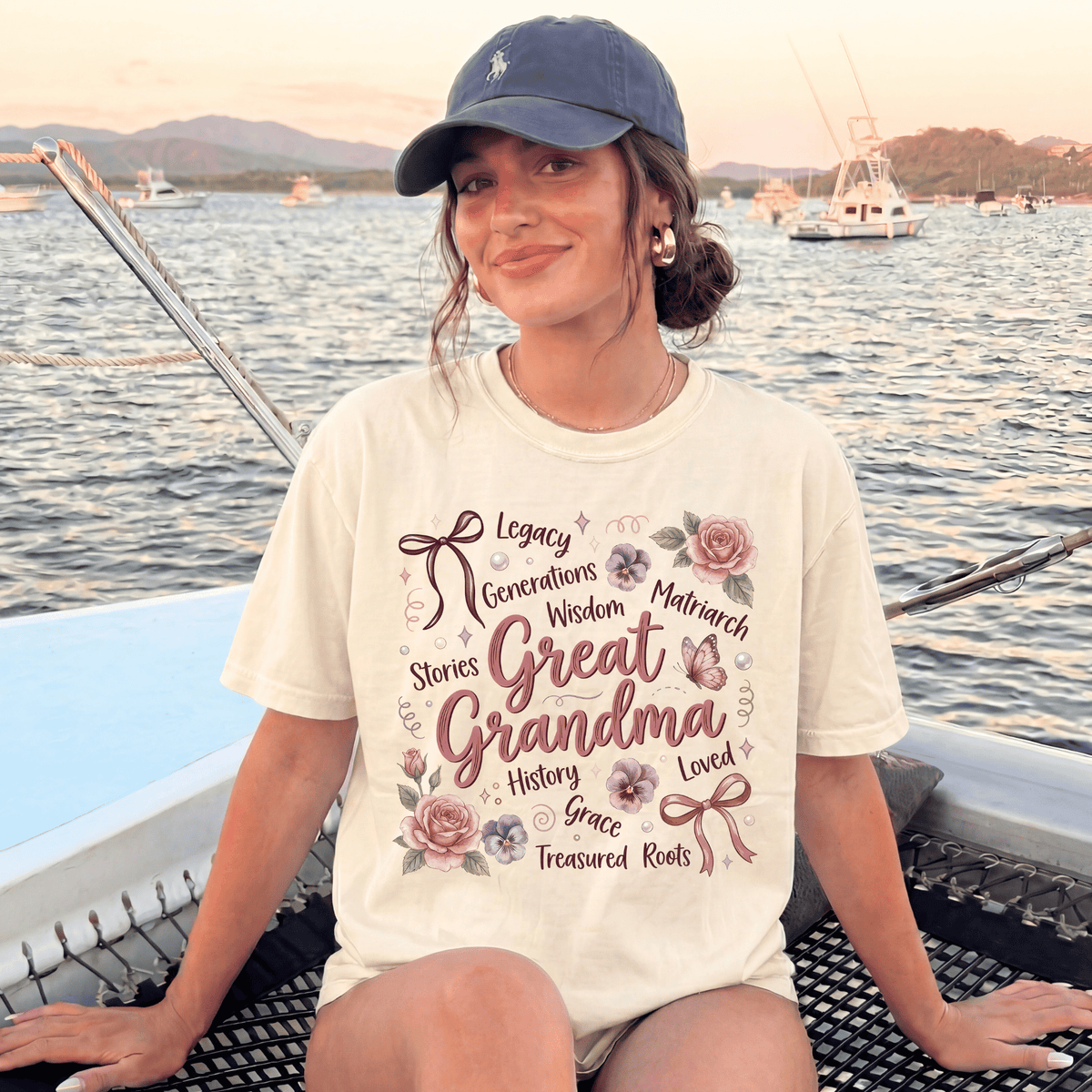 A woman wearing a white t-shirt with text and illustrations, sitting on a boat in a body of water with mountains in the background.