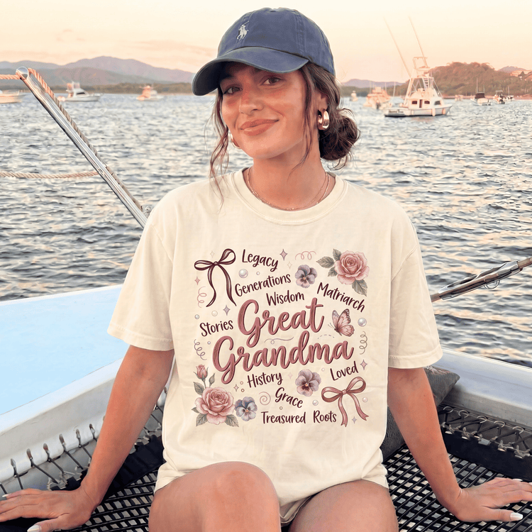 A woman wearing a white t-shirt with text and illustrations, sitting on a boat in a body of water with mountains in the background.