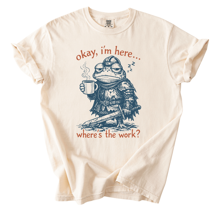 A t-shirt with a cartoon frog wearing a knight's helmet and holding a cup of coffee, with the text "okay, I'm here... where's the work?" printed on it.