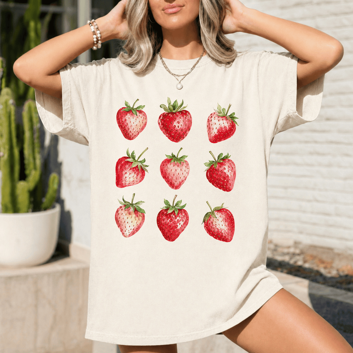 A woman wearing a white t-shirt with a graphic of nine red strawberries printed on it.