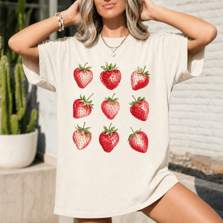A woman wearing a white t-shirt with a graphic of nine red strawberries printed on it.
