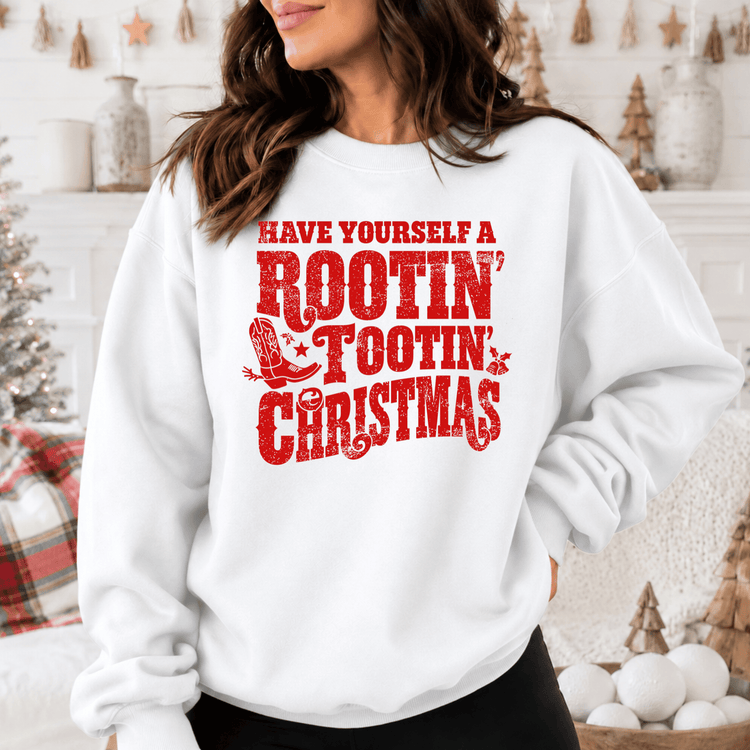 A woman wearing a white sweatshirt with a red text design that says "Have Yourself a Rootin' Tootin' Christmas".