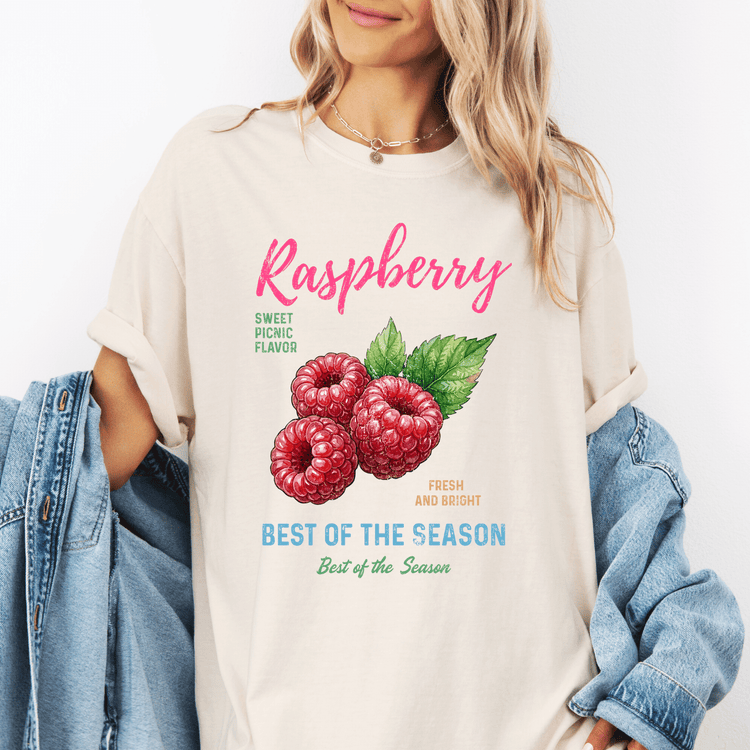 A woman wearing a white t-shirt with a graphic of raspberries and text promoting raspberry flavor.
