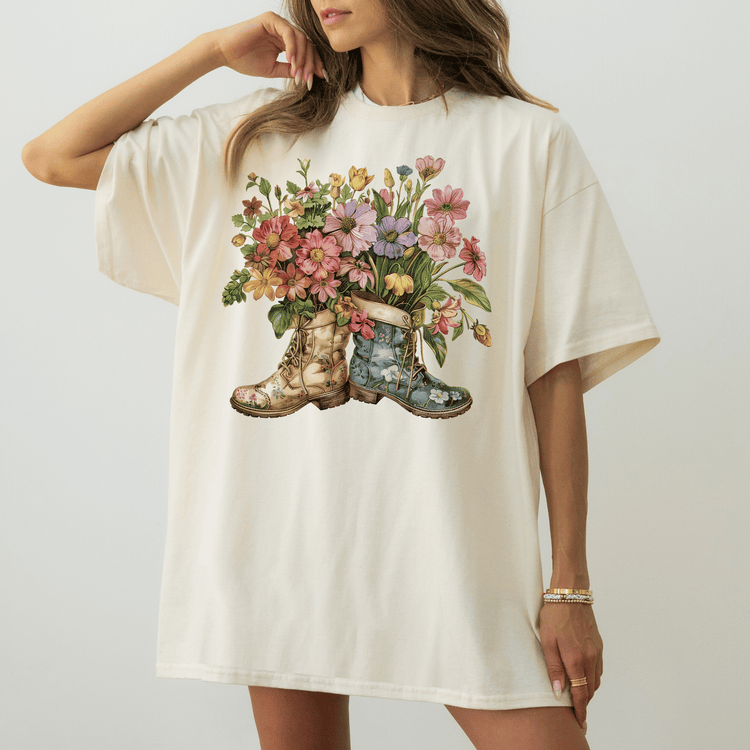 A woman wearing a white t-shirt with a floral design of two boots, one blue and one brown, holding a bouquet of colorful flowers.