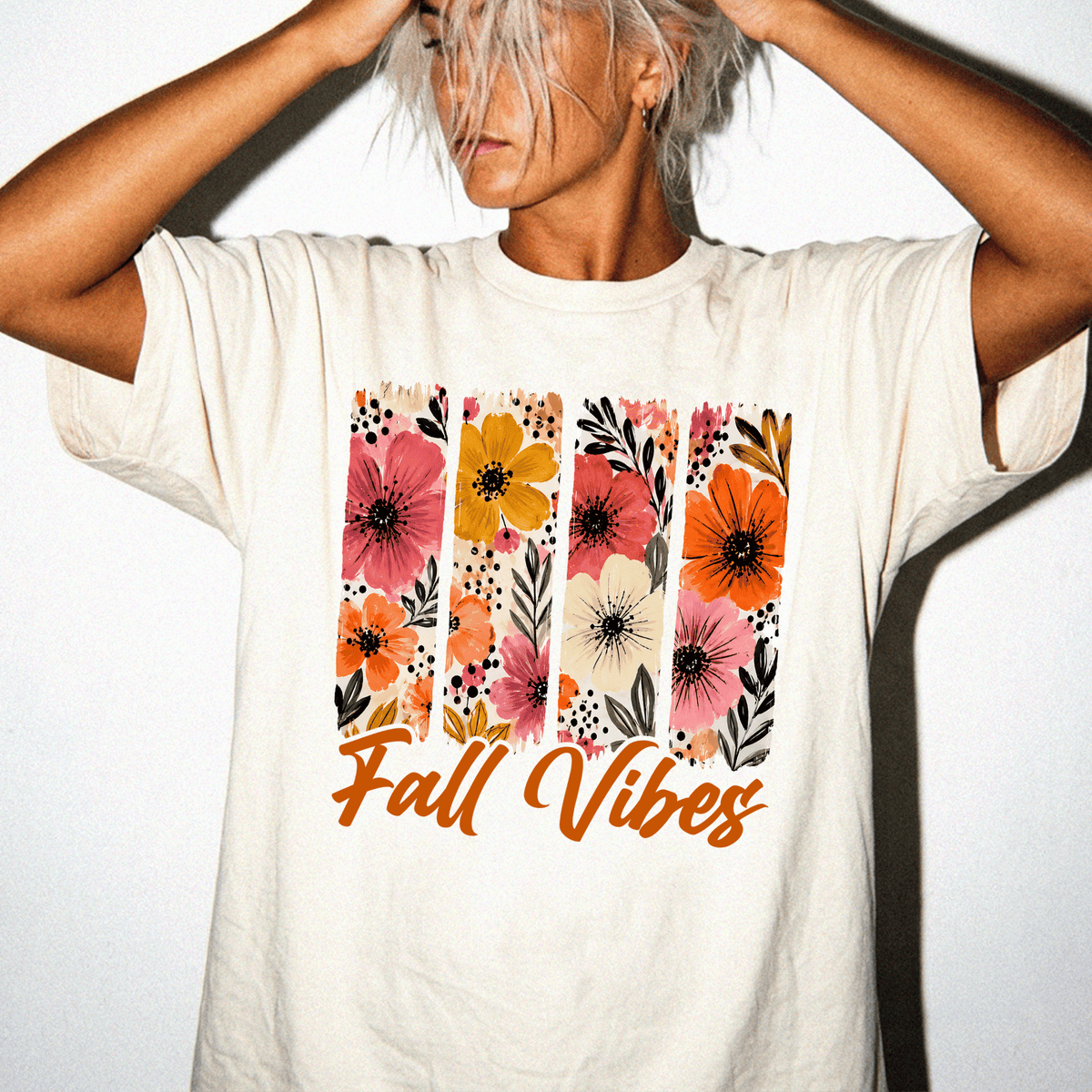 A woman wearing a white t-shirt with a floral design and the text "Fall Vibes" printed on it.
