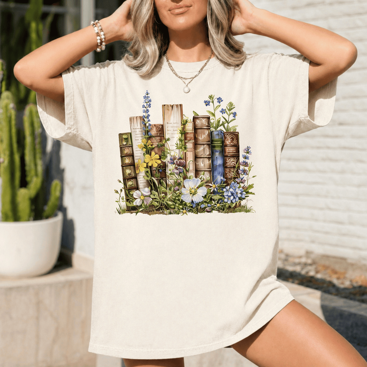 A woman wearing a white t-shirt with a printed design of books surrounded by flowers and plants.