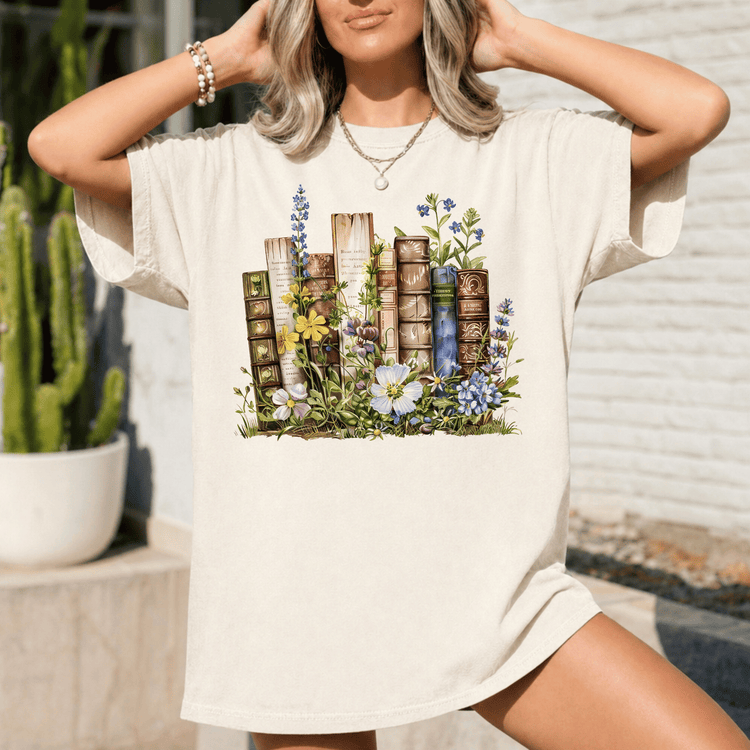 A woman wearing a white t-shirt with a printed design of books surrounded by flowers and plants.