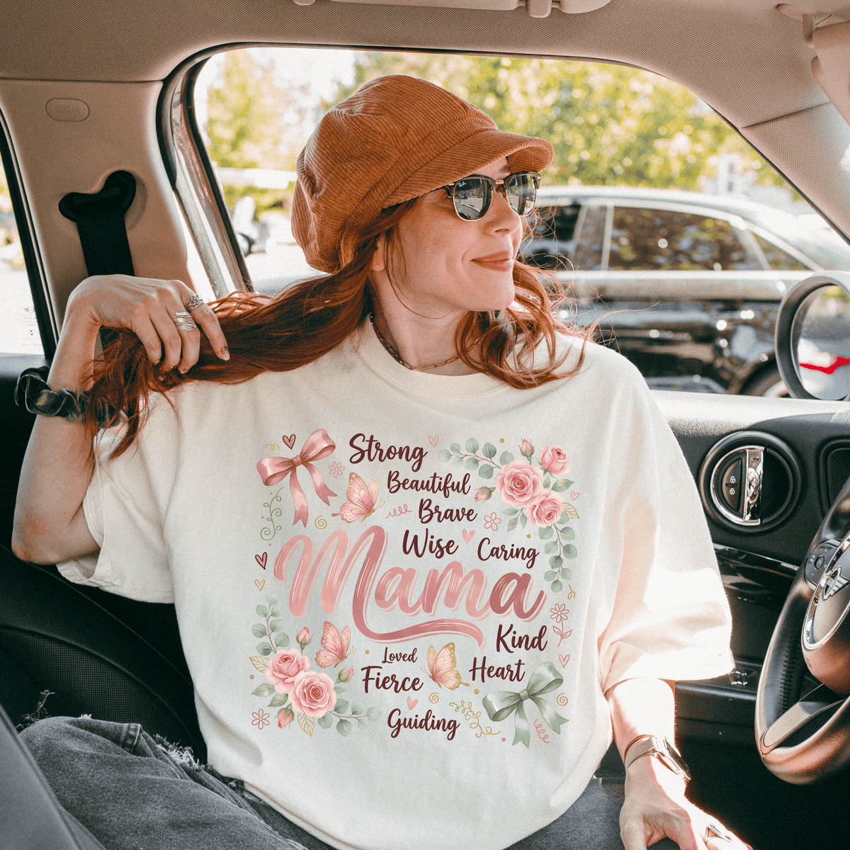 A woman wearing a white t-shirt with a floral design and text, sitting in a car.