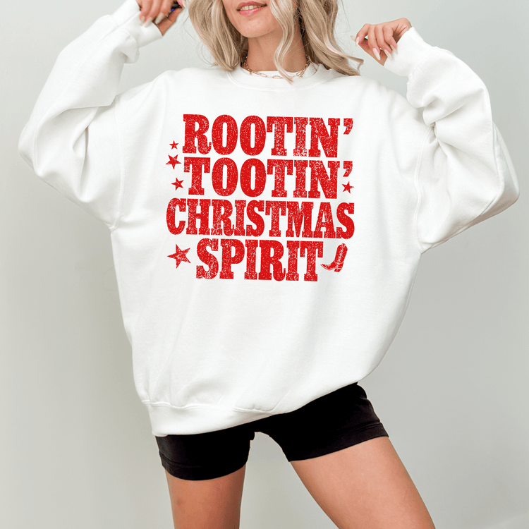 A woman wearing a white sweatshirt with a red text design that says "ROOTIN' TOOTIN' CHRISTMAS SPIRIT" printed on it.