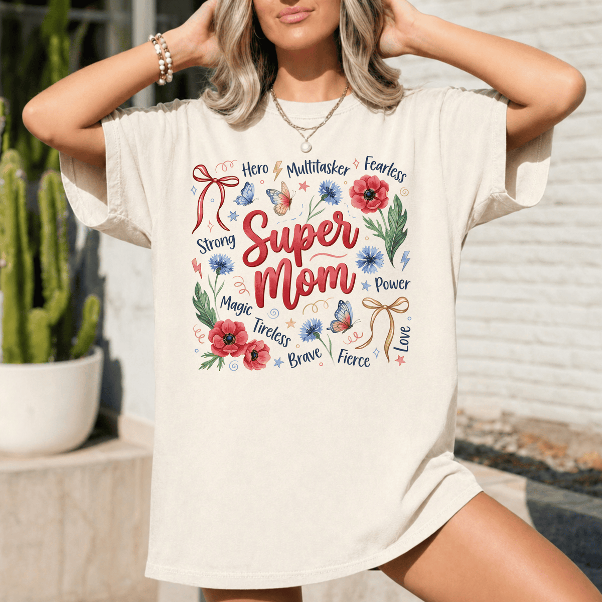A woman wearing a white t-shirt with a colorful graphic design that says "Super Mom" surrounded by various words and symbols.