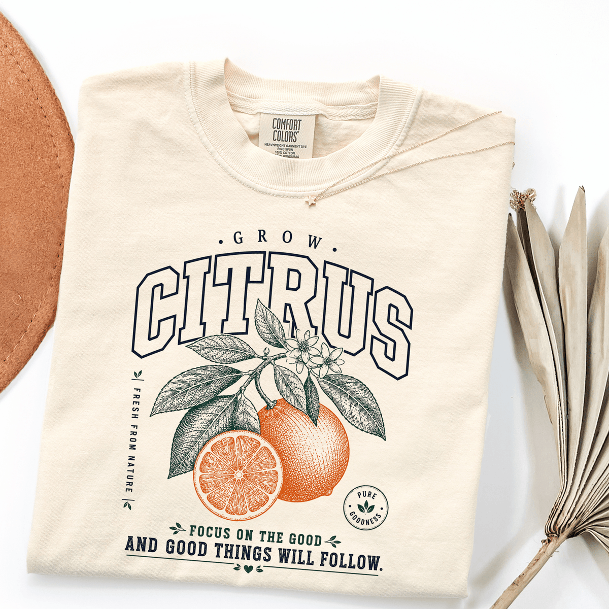 A white t-shirt with a graphic design featuring an orange and green illustration of a citrus fruit, along with the text "GROW CITRUS" and "FOCUS ON THE GOOD AND GOOD THINGS WILL FOLLOW".