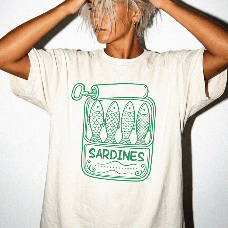 A person wearing a white t-shirt with a graphic design of four fish in a can labeled 'Sardines'.