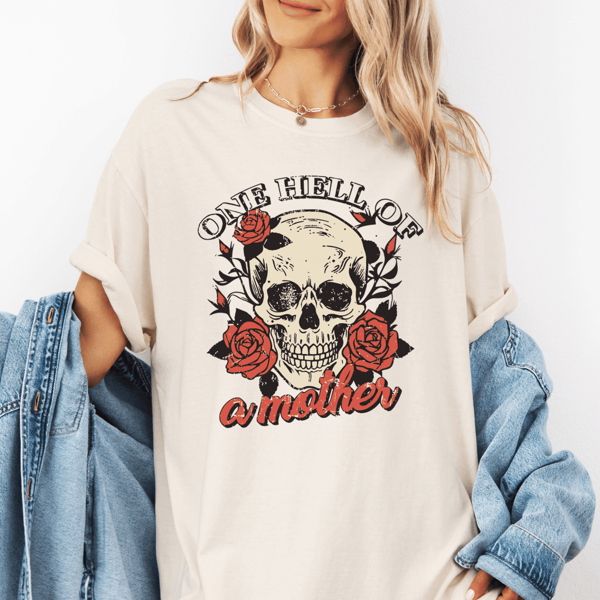 A woman wearing a white t-shirt with a skull design and the text "One Hell of a Mother" printed on it.