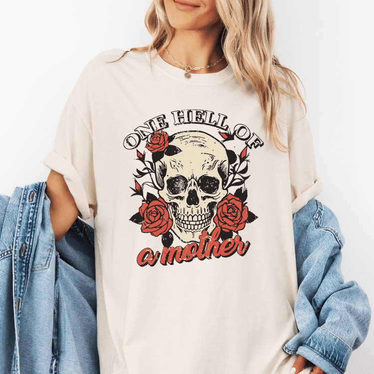 A woman wearing a white t-shirt with a skull design and the text "One Hell of a Mother" printed on it.
