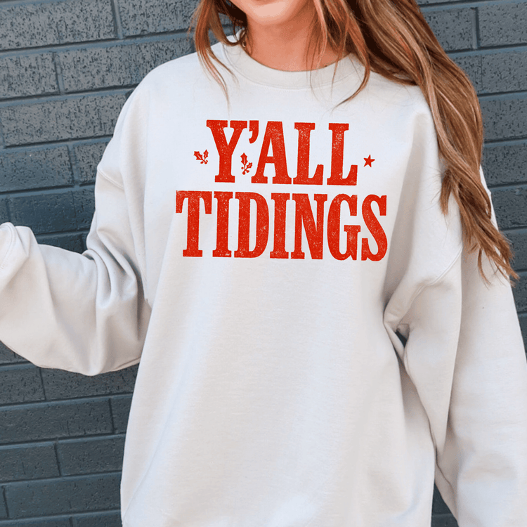 A person wearing a white sweatshirt with the text "Y'ALL TIDINGS" printed on it.