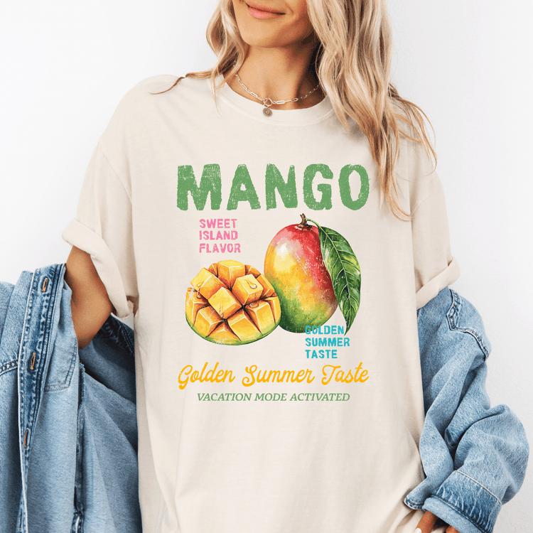 A woman wearing a white t-shirt with a graphic design featuring a mango and a leaf, along with the text "Mango Sweet Island Flavor Golden Summer Taste Vacation Mode Activated".