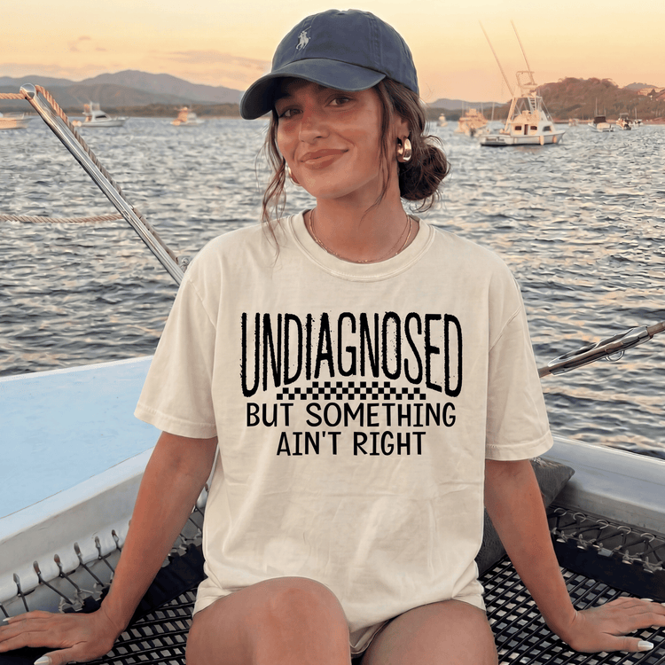 A woman wearing a white t-shirt with text and a baseball cap is sitting on a boat in the water.