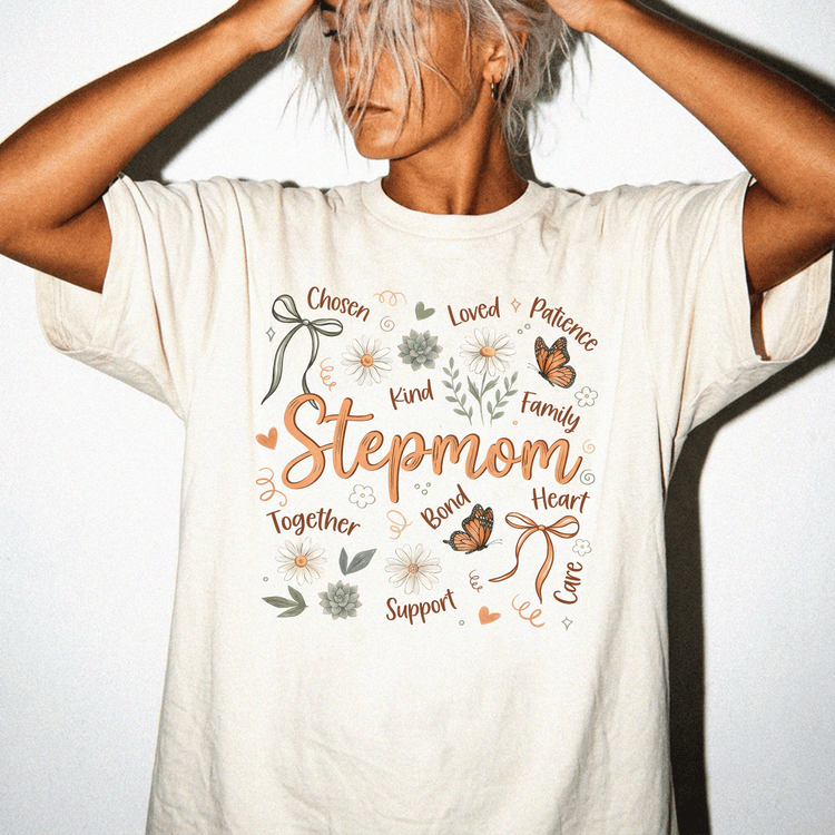 A woman wearing a white t-shirt with a graphic design featuring the word "Stepmom" surrounded by various words and illustrations such as " Chosen", "Loved", "Patience", "Kind", "Family", "Together", "Support", "Love", "CARE", and "Career".