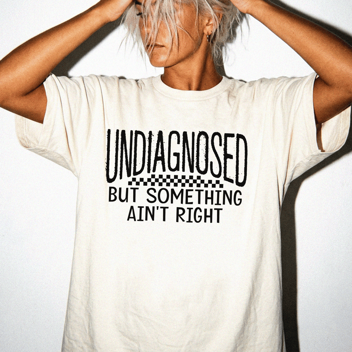 A person wearing a white t-shirt with the text "UNDIAGNOSED BUT SOMETHING AIN'T RIGHT" printed on it.
