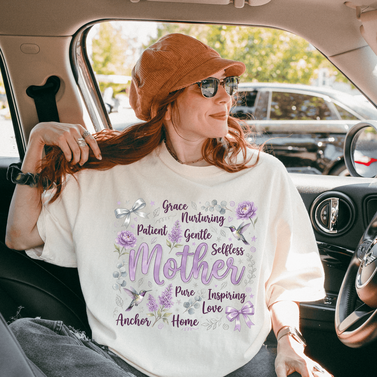 A woman wearing a white t-shirt with text and flowers on it, sitting in a car.