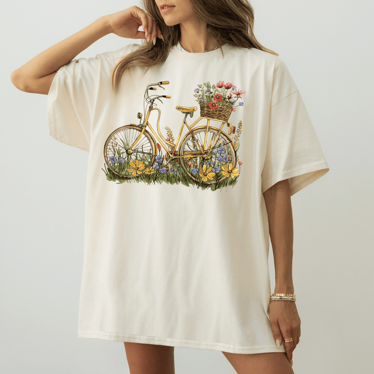 A woman wearing a white t-shirt with a bicycle graphic and flowers on the seat.