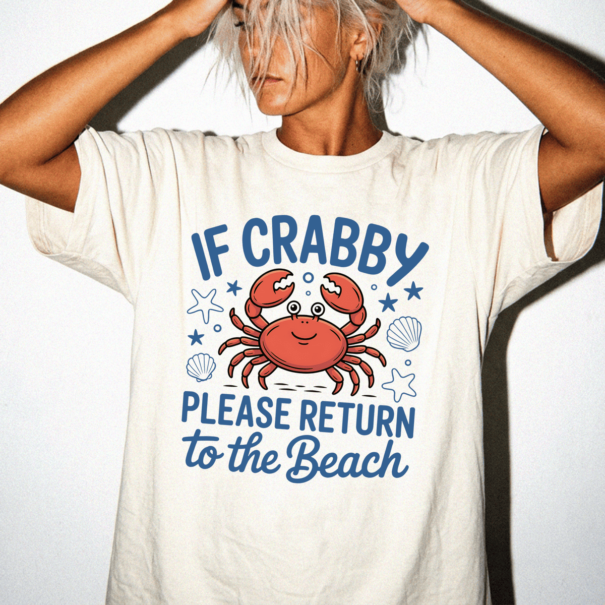A person wearing a white t-shirt with a graphic design featuring a crab and the text "IF CRABBY PLEASE RETURN TO THE BEACH".